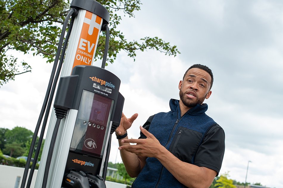 A man is outside talking in front of an electric car charging station